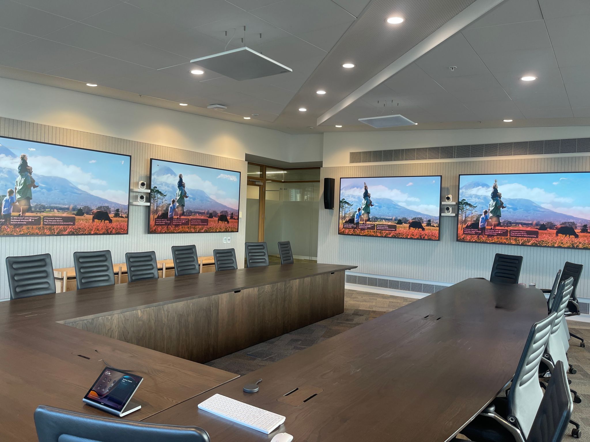 Large executive boardroom set up with a U-shaped table and four identical wall-mounted displays, demonstrating advanced audio-visual presentation capabilities.