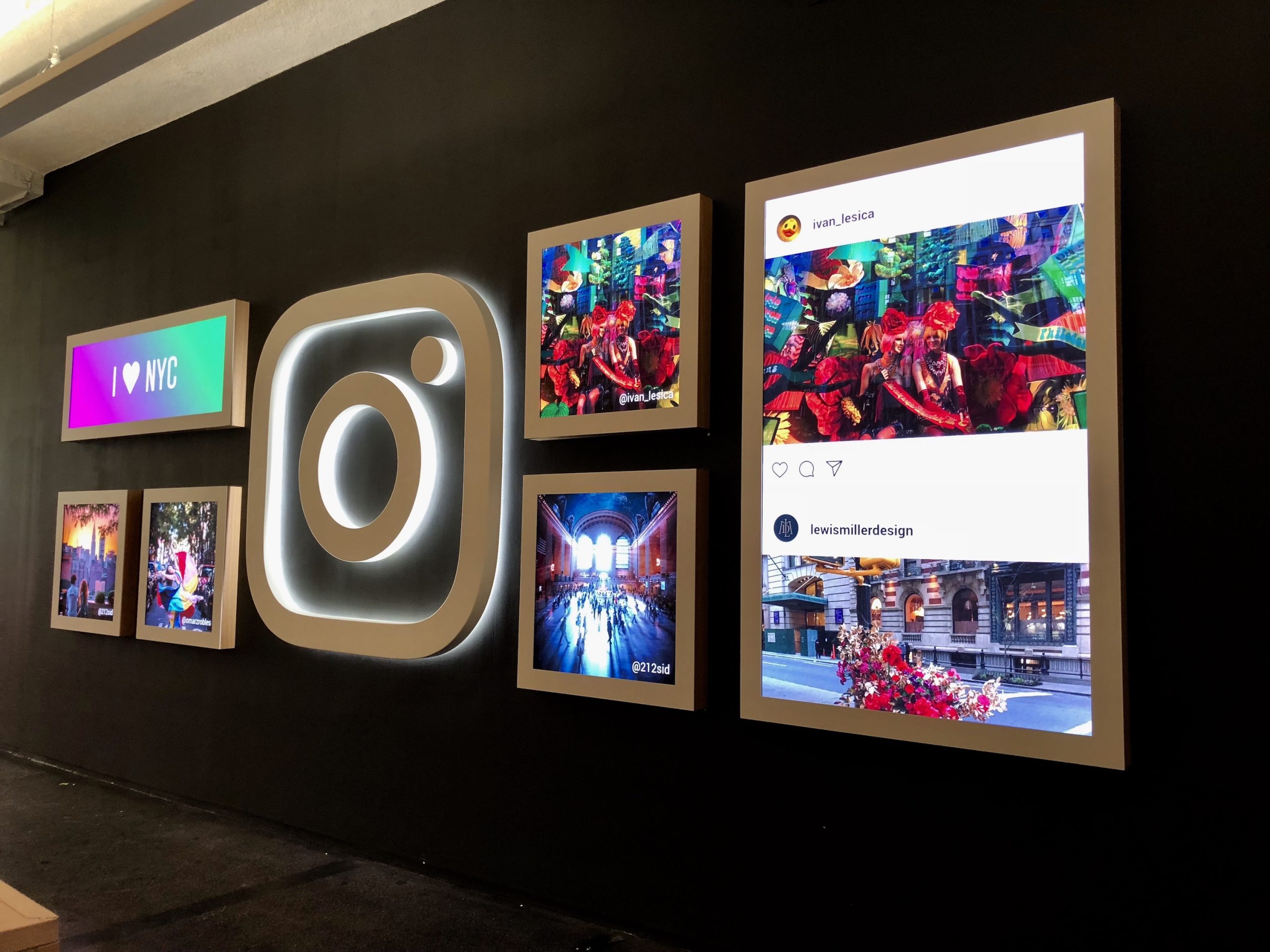 Retail wall display with a large 3D Instagram logo light surrounded by multiple digital screens showing social media posts.