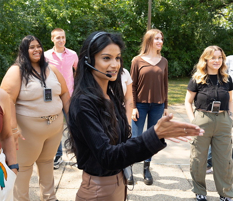 Tour guide wearing a headset and microphone gesturing to a group of people outdoors. All people in the group are wearing small personal audio receivers for a guided tour.